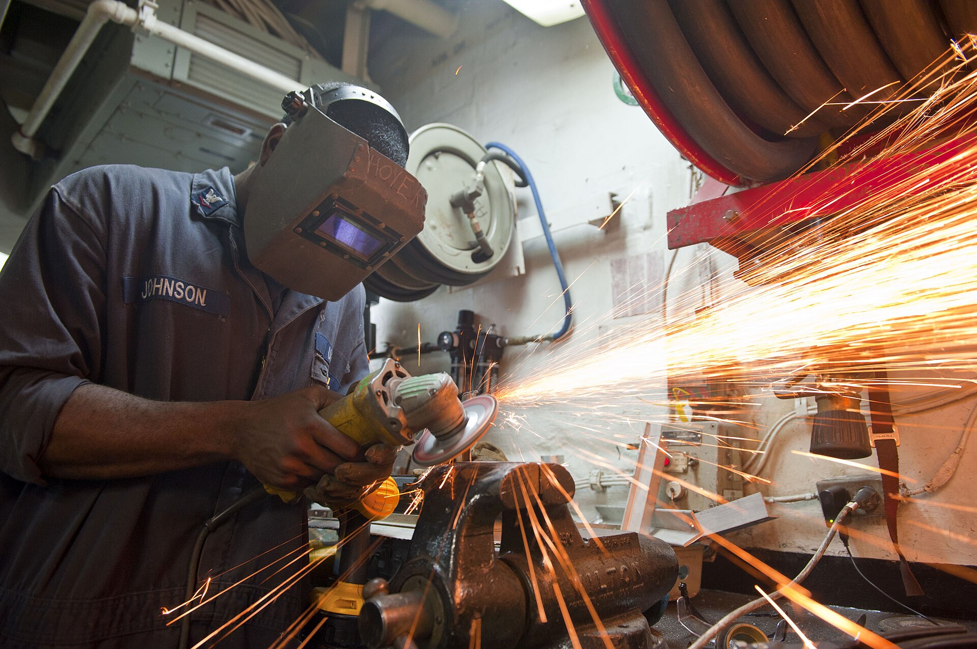 Industrial worker grinding a metal fitting in a workshop, illustrating the grinding stage in a 304 stainless steel finishing process.